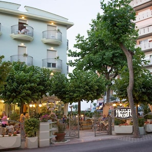 A hotel with a light blue facade, multiple balconies, and a street-level café area with outdoor seating. - Hotel Ancora (Rimini)