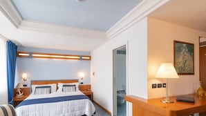 Una habitación de hotel con cama, escritorio, silla, lámpara y un cuadro en la pared.