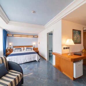A hotel room with a bed, a desk, a chair, a lamp, and a painting on the wall. - Hotel Ancora (Rimini)