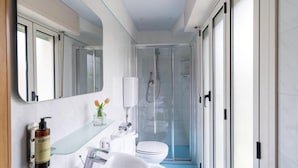 Un baño moderno con cabina de ducha de vidrio, un lavabo blanco y un inodoro.