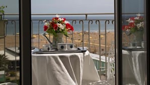 Un balcón con una mesa, un jarrón de flores y vista a la playa.
