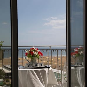 A balcony with a table, a vase of flowers, and a view of the beach. - Hotel Ancora (Rimini)
