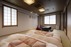 Habitació d'estil japonès tradicional amb fusteria de tatami, dos llits amb roba de llit estampada, una taula petita i un televisor.