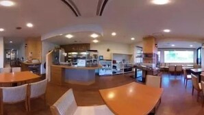 Ein Restaurantinneres mit mehreren Sitzbereichen, einer zentralen Theke und einem an der Wand montierten Fernseher.