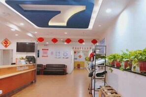 Ein Hotel-Empfangsbereich mit einer Rezeption, Sitzgelegenheiten und einem an der Wand befestigten Fernseher.