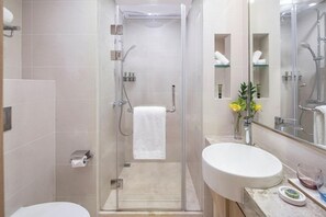 A modern bathroom with a glass-enclosed shower, a white sink, and a mirror with a glass shelf.