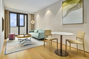 Moderni hotellihuone, jossa on sohva, pyöreä pöytä ja kaksi tuolia.