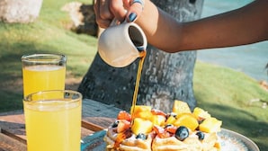 Una persona vertiendo jarabe sobre una porción de waffles con fruta.