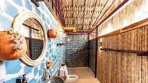 Un baño con pared de piedra, puerta de madera, inodoro blanco y un lavabo grande.
