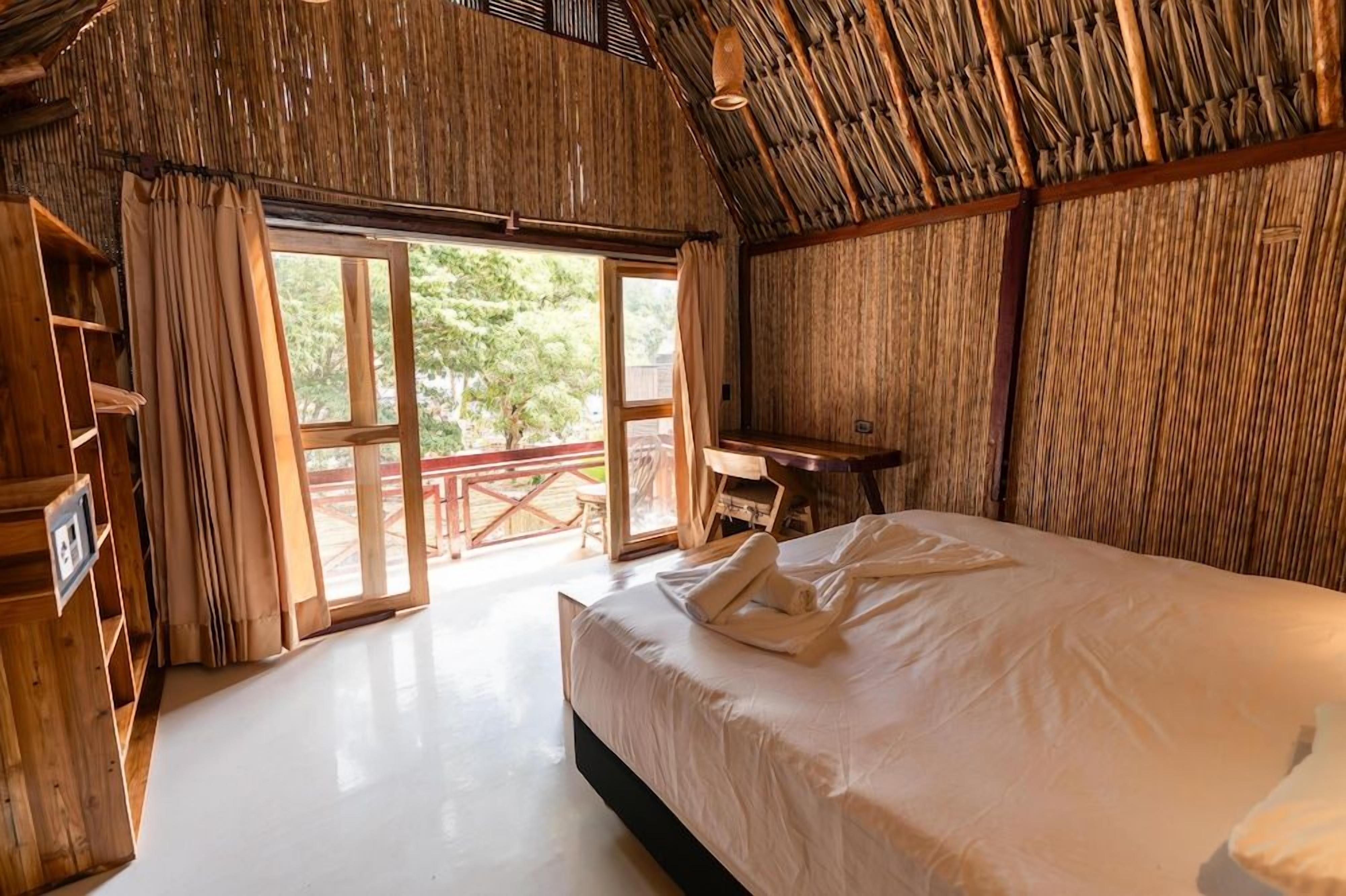 Una habitación con una cama, un escritorio de madera y un ventanal amplio.