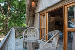 Un edificio de madera con techo de paja, un área de estar al aire libre techada con sillas de mimbre y vista a un paisaje natural.