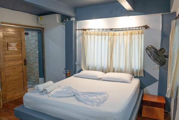 Una habitación de hotel con una cama, una puerta de madera, una cortina, un ventilador y un cartel en la pared.