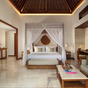 A bedroom with a canopy bed, a wooden headboard, a bedside table with a lamp, and a coffee table with books.