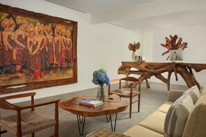 A room with a large traditional painting, a wooden coffee table with books, a vase with flowers, and a unique wooden chair.