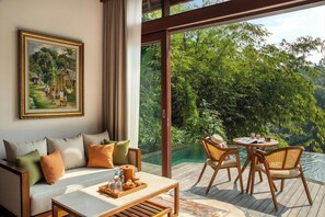 A room with a sofa, a table, and a view of a lush garden through a glass door.