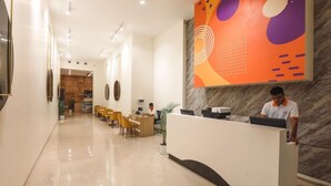 Ein Hotel-Empfangsbereich mit einer Marmor-Rezeption, einer Sitzecke mit Stühlen und einem großen, abstrakten Wandkunstwerk.