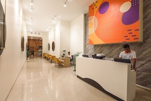 Uma área de recepção de hotel com um balcão de mármore, espaço de estar com cadeiras e uma grande obra de arte abstrata na parede.