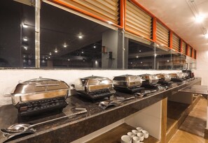 A buffet setup with multiple self-service stations, including hot and cold food options, and a variety of serving utensils. - IRA by Orchid Sambhajinagar (Chhatrapati Sambhajinagar)