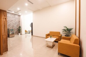 A modern lobby with a marble wall, a vending machine, a seating area with a sofa and a coffee table, and a potted plant. - IRA by Orchid Sambhajinagar (Chhatrapati Sambhajinagar)