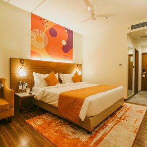 Una habitación de hotel con una cama, una mesita de noche, una silla, un ventilador de techo y una obra de arte en la pared.