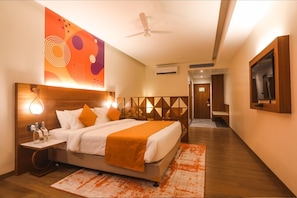 Quarto de hotel com cama, mesa de cabeceira e televisão presa na parede.
