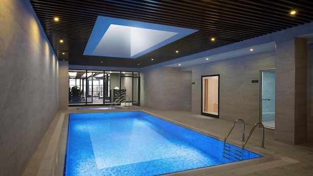 Una piscina interior con tragaluz, una puerta de cristal y vistas a un gimnasio.