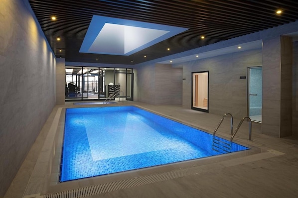 Una piscina interior amb un fanal i una porta de vidre, amb vistes a una zona de gimnàs.