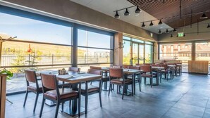 Un comedor amplio con varias mesas y sillas, ventanas grandes que ofrecen vistas al exterior, y un diseño moderno de techo.