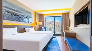 Habitación de hotel con dos camas, un escritorio, un televisor y vista a las montañas.