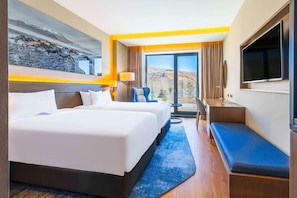 Habitació d'hotel amb dos llits, un escriptori, un televisor i vistes a les muntanyes.