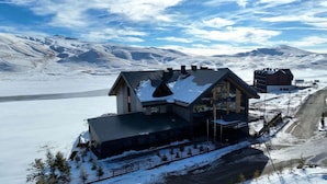 Un edificio moderno con un amplio frente de cristal, ubicado en un paisaje nevado con montañas al fondo.