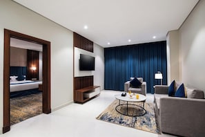 A modern hotel room with a bed, a TV, a sofa, a coffee table, and a large window with curtains.