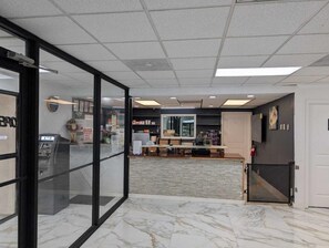 Un vestíbulo con mostrador de recepción, puerta de cristal y cajero automático.