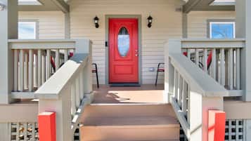 A front porch with a red door, two steps leading up to it, and a small porch area with a chair.
