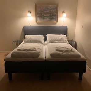 Cama doble con dos mesitas de noche, cada una con una lámpara, en una habitación con un cuadro en la pared.