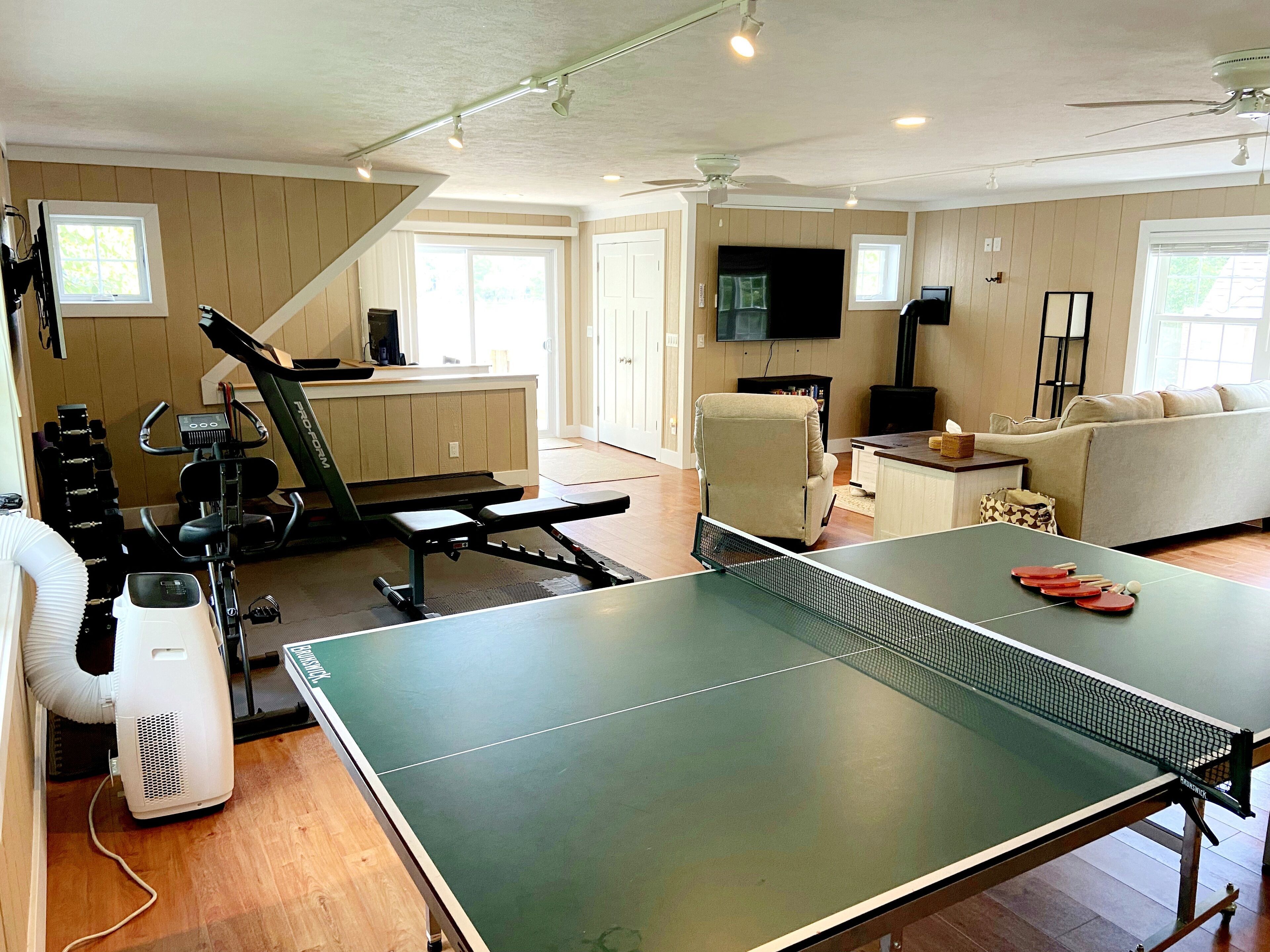 A living room with a ping pong table, exercise equipment, a sofa, and a television.