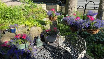 Een tuin met verschillende planten in potten, een Boeddhabeeld en een metalen bank.