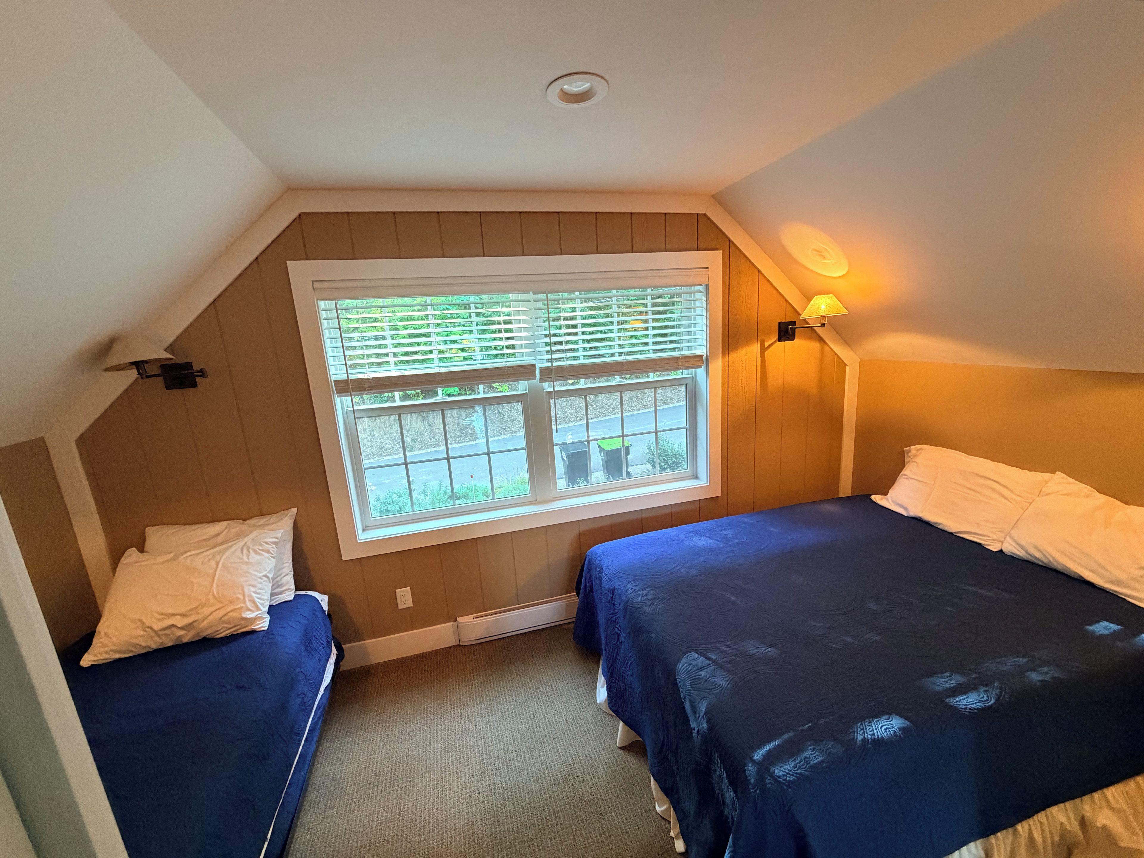 Ein Schlafzimmer mit zwei Betten, einem Fenster mit Jalousien, einer Wandlampe und einer Deckenleuchte.