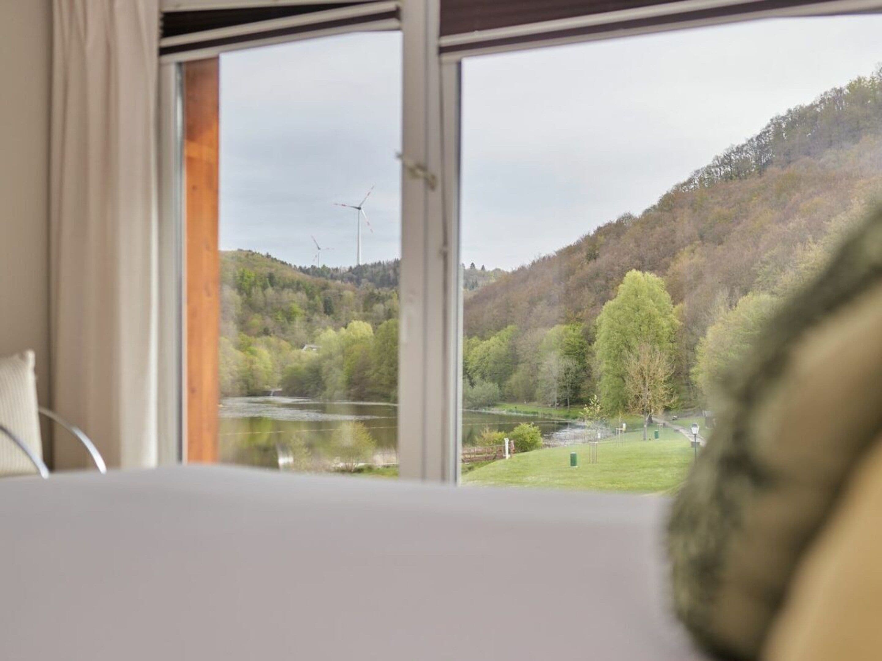 A room with a large window overlooking a lake and a forested hillside.