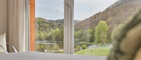 A room with a large window overlooking a lake and a forested hillside.