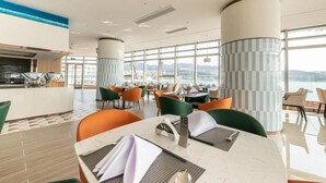Um restaurante moderno com teto alto, grandes janelas e vista para o mar.