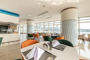 Un ristorante moderno con soffitto alto, ampie finestre e vista sul mare.