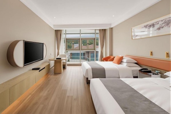 Habitación de hotel con una amplia televisión de pantalla plana, dos camas, un escritorio y ventana con vistas a edificios.