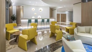 Um saguão moderno com balcão de recepção, assentos em amarelo e branco e piso de mármore.
