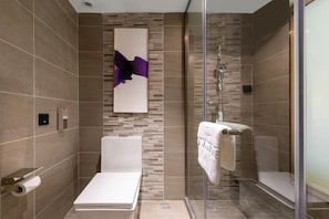 A modern bathroom with a glass shower enclosure, a white bathtub, and a wall-mounted abstract art piece. - Lavande Hotel (Zhuhai)