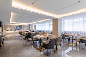 A modern dining area with tables and chairs, a kitchen in the background, and large windows. - Lavande Hotel (Zhuhai)