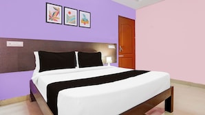 A bed with a black and white bedspread in a room with purple walls and a wooden door. - OYO Hotel O Karakambadi Near Alipiri (Tirupati)