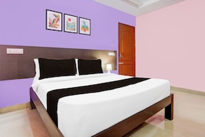Uma cama com colcha preta e branca em quarto com paredes roxas e porta de madeira.