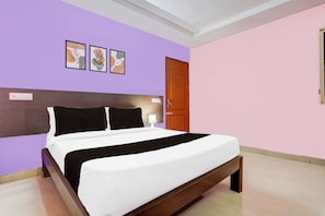 Quarto de hotel com cama, cabeceira de madeira, porta e parede com três quadros.