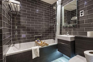 Un baño moderno con una pared de azulejos oscuros, una bañera, un box de ducha con mampara de cristal y un tocador con espejo.